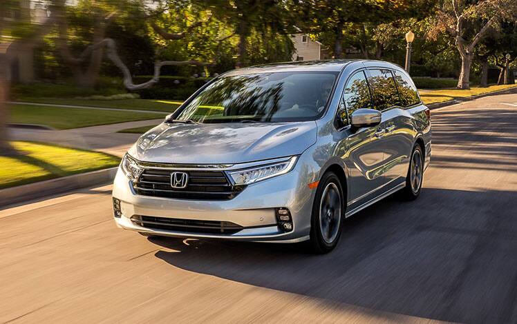 Front driver-side view of the 2022 Honda Odyssey Elite in Lunar Silver Metallic driving on a residential street.
