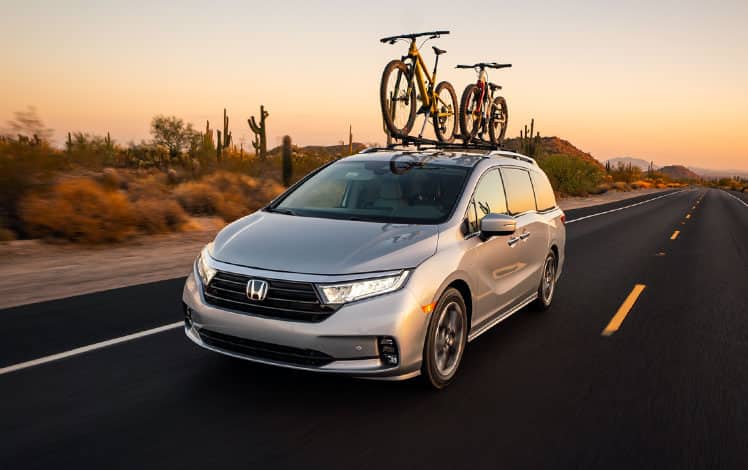 Front driver-side view of the 2022 Honda Odyssey Elite in Lunar Silver Metallic with Honda Genuine Accessories, driving in the desert with two bikes on rooftop.