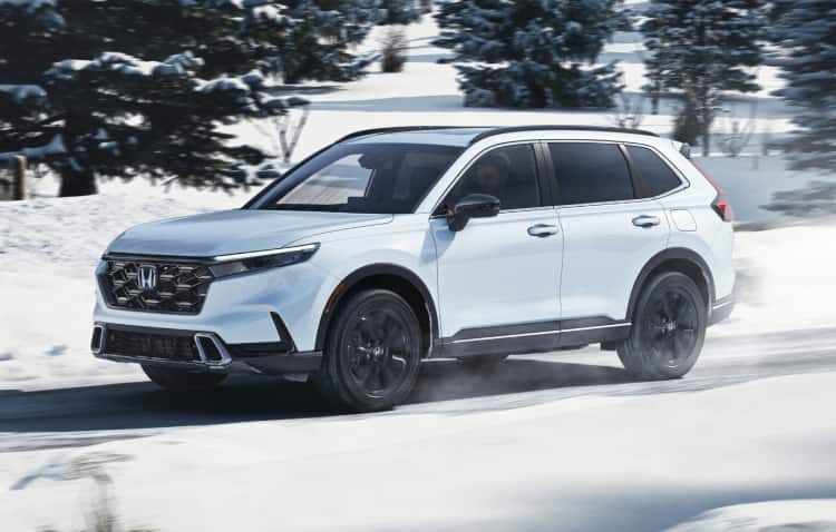 Side front view of 2025 CR-V Sport AWD in Platinum White Pearl driving on a snowy mountain road.